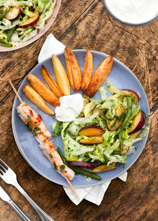 Koteletter på spyd serveret med sprøde kartofler og blommesalat