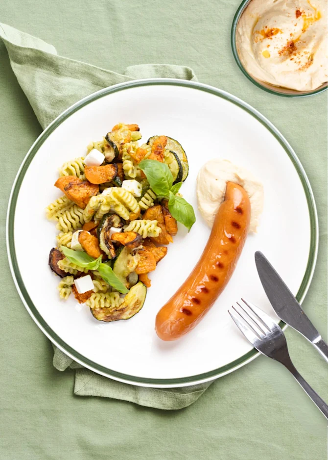 Grillpølser serveret med pastasalat, søde kartofler og pesto. Hertil hummus