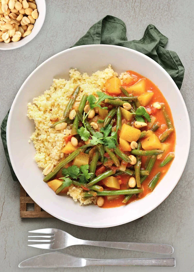 Vegetarisk gryderet med kartofler, bønner og kokosmælk. Hertil bulgur og peanuts