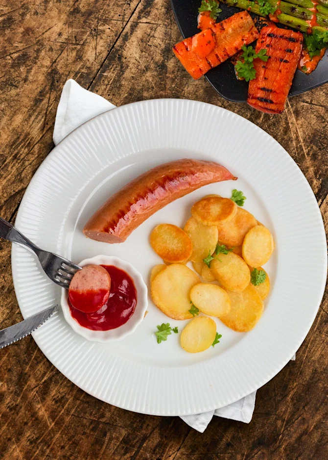 Grillede pølser med kartoffelskiver. Hertil grillede asparges og gulerødder