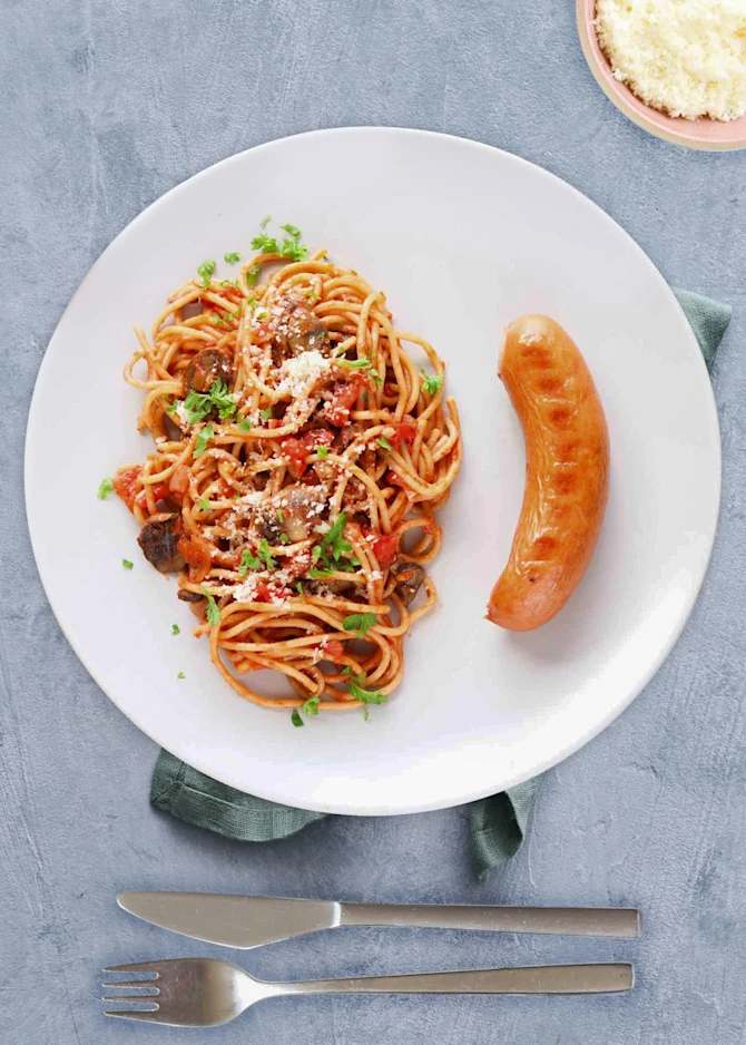Grillpølser serveret med spaghetti vendt i tomatsauce med champignoner