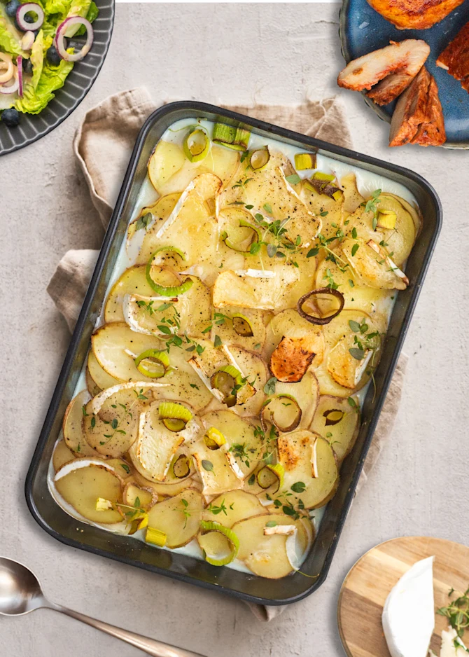 Saftige kyllingestykker i fad med kartofler, porre og brieost. Hertil blåbærsalat